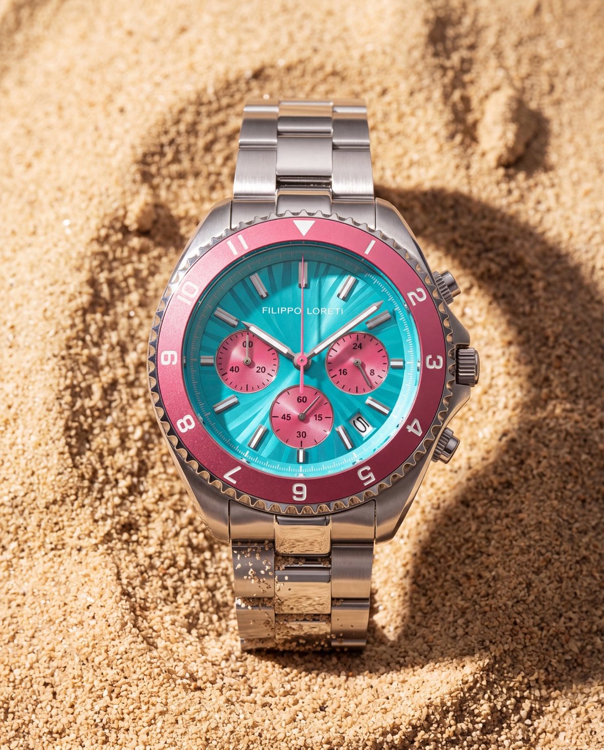 The Ascari Miami lying face up in warm sand, its turquoise dial and pink bezel in bright sun