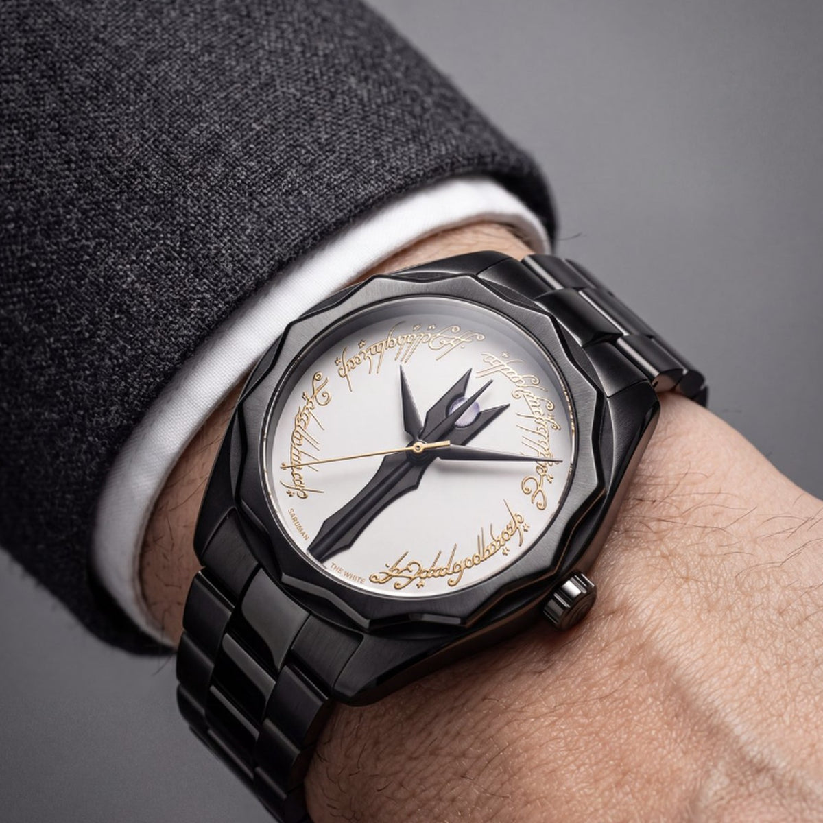 The Saruman watch worn on the wrist on its black steel bracelet, below a tailored jacket cuff and white shirt
